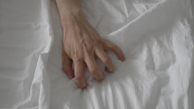 4K close-up video of an unrecognizable person's hand gripping a white bed sheet tightly, symbolizing an intense moment of climax.Conceptual footage about safe sex, sexual pleasure, consent, and sexual