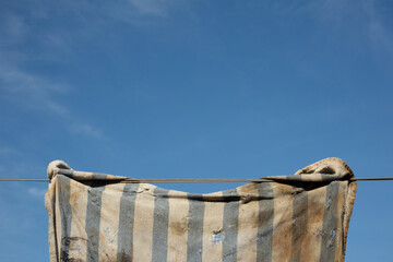 A fragment of a dirty, torn rag hanging on a string. Blue sky in the background.                 F