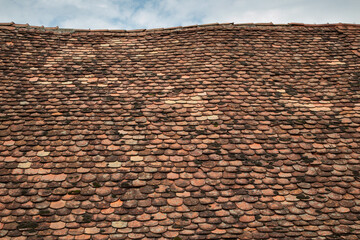 An old, undulating roof with old tiles, with a fragment of the sky with clouds in the background.