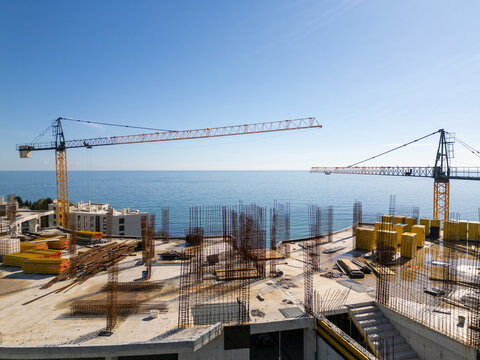 Aerial view of a construction site with tower cranes building modern apartments near the sea coast on a sunny day. Urban development concept