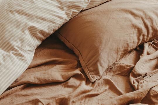 Cozy bed with rumpled linen sheets and striped pillow in warm tones