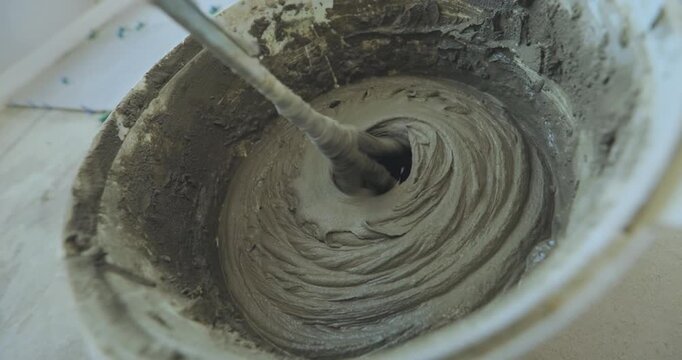 A man kneads tile mortar in a bucket with a paddle mixer or a paddle mixing drill. Mixing tile mortar for laying ceramic tiles or porcelain tiles.