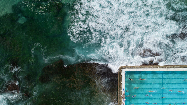 Aerial view of the Bondi Icebergs Club pool with swimmers, where the blue ocean meets a man-made rectangular pool, Sydney, New South Wales, Australia.