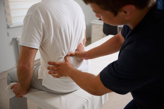 Chiropractor performing manual back adjustment on patient in medical clinic. Physiotherapy, spinal alignment, and rehabilitation treatment for lower back pain relief. - Powered by Adobe