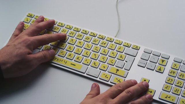 Computer keyboard with braille font alphabet. Blind person is typing words, hands. Technological device for visually impaired people. Tactilely touches bumps on keys. Inclusion, assistive technology
