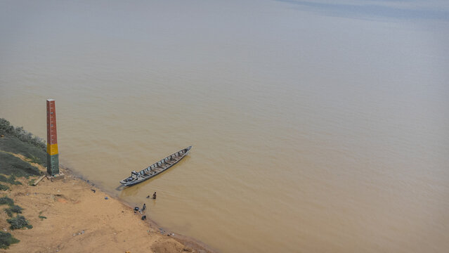 Aerial view of a boat resting on the muddy bank of the river, with a tall, weathered navigational marker looming beside it, Makurdi, Benue, Nigeria.