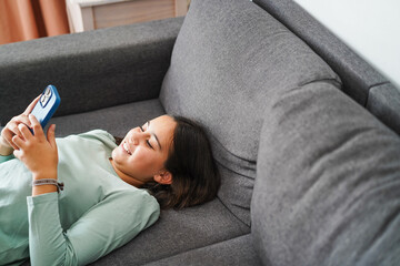 Female teen using smartphone at home on sofa - Technology and teenager lifestyle concept - Main focus on face