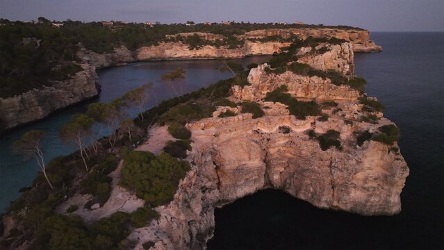 Aerial view of rugged cliffs embrace the turquoise cove, fringed by verdant trees against the deep blue sea, creating a dramatic coastal vista, Cala des Moro, Balearic Islands, Spain.