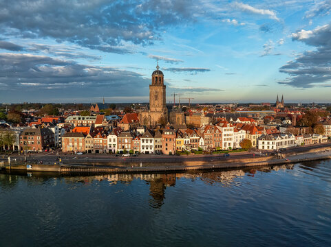 Aerial view of the Lebuinus Church standing tall amidst a tapestry of historic buildings reflected in the tranquil waters of the IJssel River, Deventer, Overijssel, Netherlands.