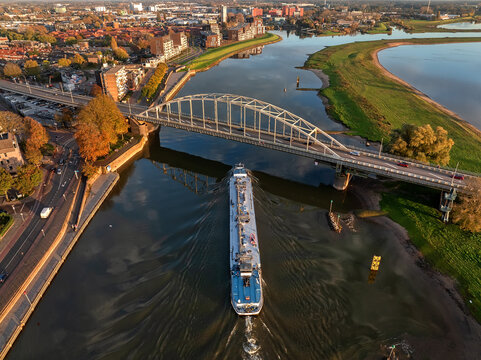 Aerial view of a long barge sailing under the Wilhelminabrug bridge reflecting in the still waters of the IJssel river, Deventer, Overijssel, Netherlands.