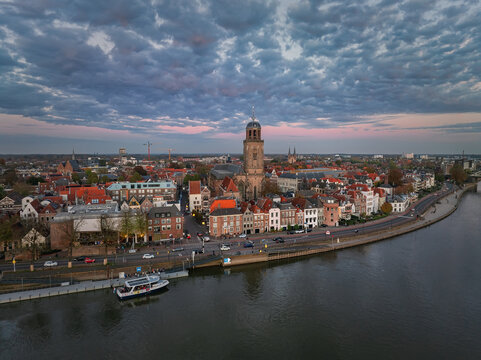 Aerial view of the Lebuinus Church soaring over the red-tiled roofs, with the IJssel River reflecting the pastel sky at twilight, Deventer, Overijssel, Netherlands.