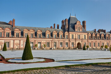 View of Fontainebleau Palace with classical architecture and gardens protected from the cold under a blue sky