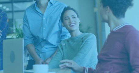 Smiling mid adult Hispanic woman speaking to colleagues at office desk, with laptop and coffee mug