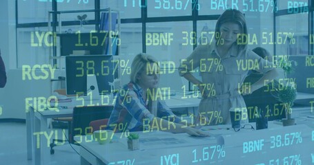 Reviewing two women leaning over printed schematics at open-plan desk, with ticker overlay