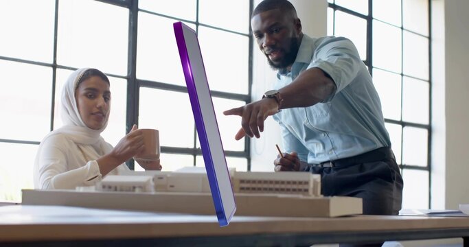 Collaborating woman wearing headscarf and man examining model with digital display in design studio