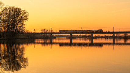 Naklejka premium Train crossing bridge at sunset over calm water