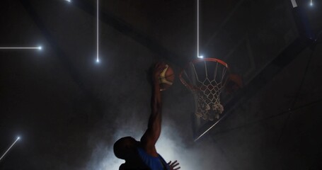 Leaping athlete executing slam dunk in dim gym, with basketball, hoop, fog and light beams © vectorfusionart