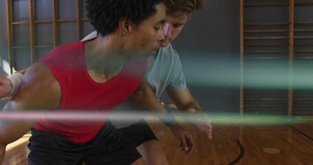 Two athletes practicing basketball drill in school gym, taking defensive stance with wall bars