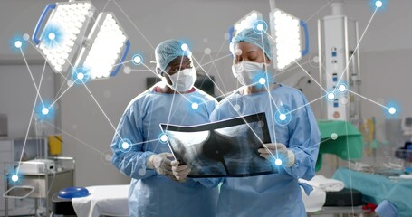 Two surgeons wearing scrubs reviewing chest X-ray film in operating room, with surgical lights