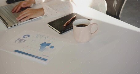 Typing adult worker hands on silver laptop at office desk, with printed report and coffee mug