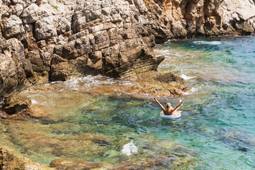 Woman relaxing on an inflatable ring in the clear turquoise Mediterranean sea near the rocky coast of Saint-Jean-Cap-Ferrat, France.