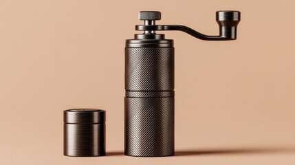 A close up studio shot of a dark metal manual coffee grinder with a patterned texture next to its small container against a plain beige background.