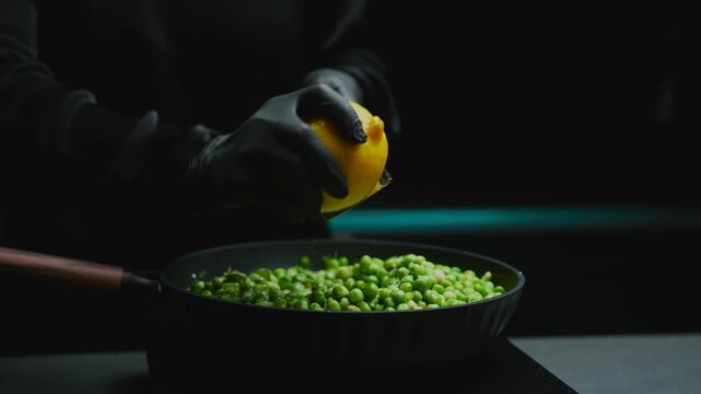 Chef hands in black gloves grating fresh lemon zest into a pan of bright green peas, preparing a delicious gourmet meal with fresh ingredients and healthy spices