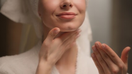 Happy beautiful Caucasian young woman applying body cream rubbing neck skincare gorgeous female model in bath towel bathrobe apply lotion cosmetic massaging soft skin care beauty routine home bathroom
