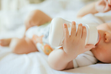 baby drinks milk from bottle lying on bed in nursery room.