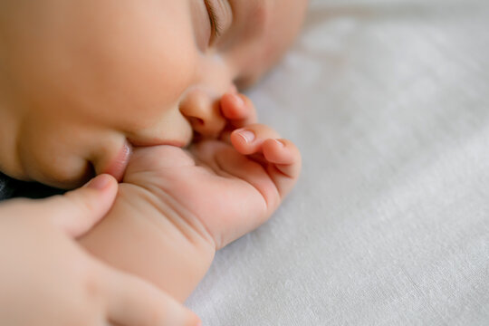 baby sucking his thumb on white bedding while sleeping