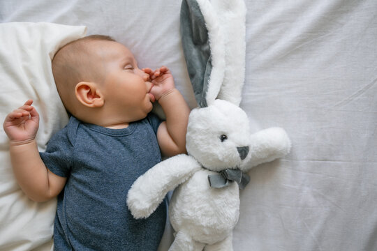 Sleeping cute baby boy sucking thumb finger with plush bunny rabbit toy on white blanket