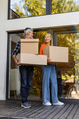 Senior couple carrying boxes together at home porch smiling