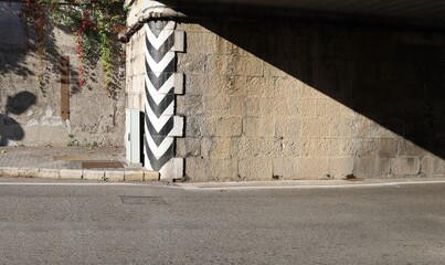 Vertical black and white road markings at the entry of an old road tunnel made of stone block . Sidewalk on the left, street in front. Background for copy space.