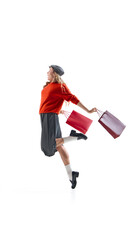 Young fashionable woman posing with red shopping bags in playful motion on white background. Concept of retail lifestyle, elegance, femininity, and cheerful emotion for advertising campaigns.