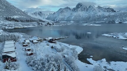 Aerial view of snow-laden mountains meeting the tranquil lake waters, creating a serene contrast of textures and tones, Lofoten, Norway. - Powered by Adobe