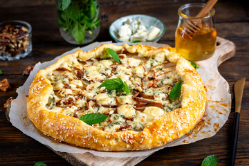 Baked galette or open pie with pear, blue cheese and nuts on the wooden table.