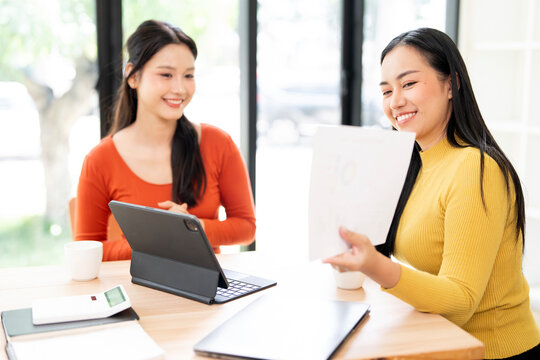 Two cheerful Asian businesswomen reviewing financial documents and collaborating on a project.