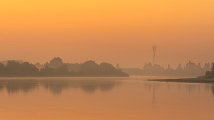 Misty river at sunrise with power lines
