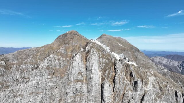Aerial view of the rugged Apuan Alps, showcasing contrasting textures of grey rock and sparse vegetation under a clear blue sky, Levigliani, Toscana, Italy.