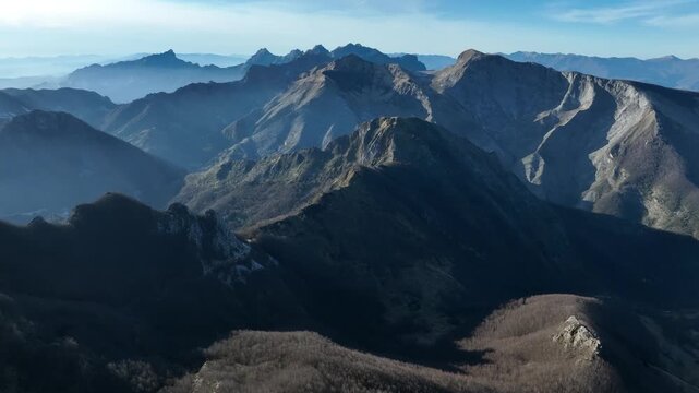 Aerial view of jagged mountain peaks reach for the sky, casting shadows across the rugged landscape near Levigliani, Toscana, Italy.