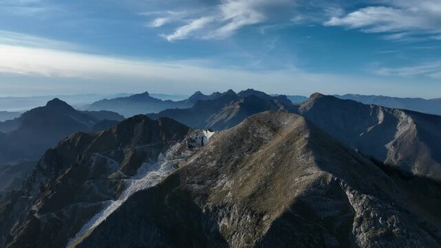 Aerial view of the stark white marble quarries contrasting against the rugged, dark mountains under a serene sky, Levigliani, Toscana, Italy.