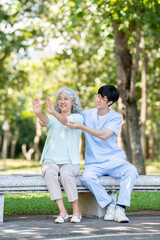 Naklejka premium Asian man caregiver nurse helping old woman grandmother patient exercising sitting on bench in park.