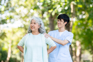 Glasses asian man caregiver nurse shoulder massaging old woman granny patient while standing in park