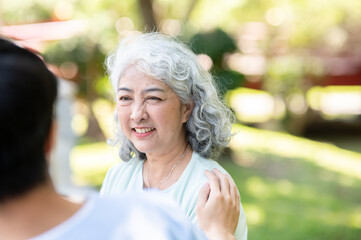 Young man caregiver nurse holding patting shoulder of old woman granny patient while sitting in park