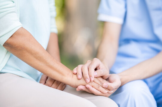 Close up of young caregiver nurse holding hands comforting old woman grandma patient sitting in park