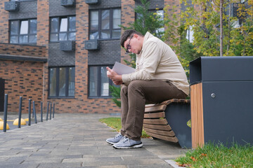 A handsome guy looks, reading a book sitting on the bench in the urban park