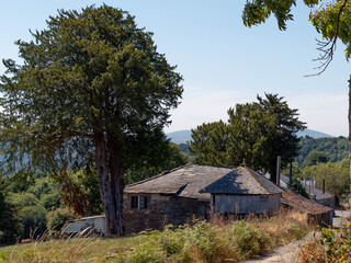 Stone houses in the mountains of A Fonsagrada, Lugo, Galicia, Spain. Traditional Galician mountain village with stone walls wooden details and black slate roofs on a sunny day in northern Spain.