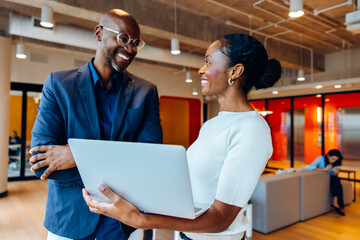 Two professionals discussing work while smiling together in a shared office space