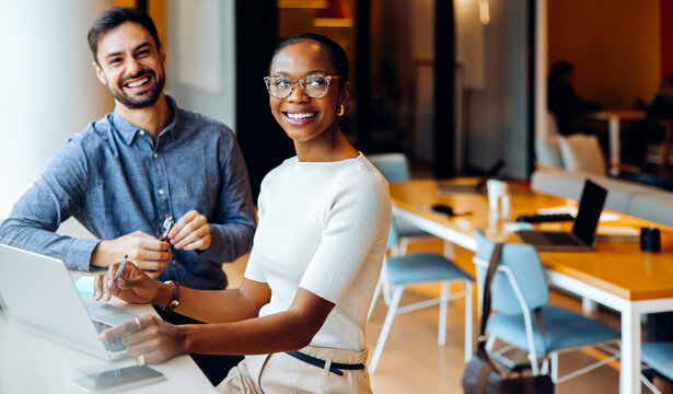 Two office colleagues smiling and working at a laptop computer in a shared space