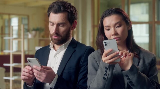 Multiethnic business colleagues using devices at office Korean businesswoman scrolling mobile phone thoughtful envious glancing coworker screen Caucasian man checks online networking browsing internet